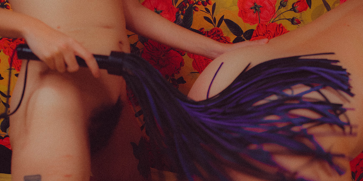 A Queer Person using a flogger on another queer trans person