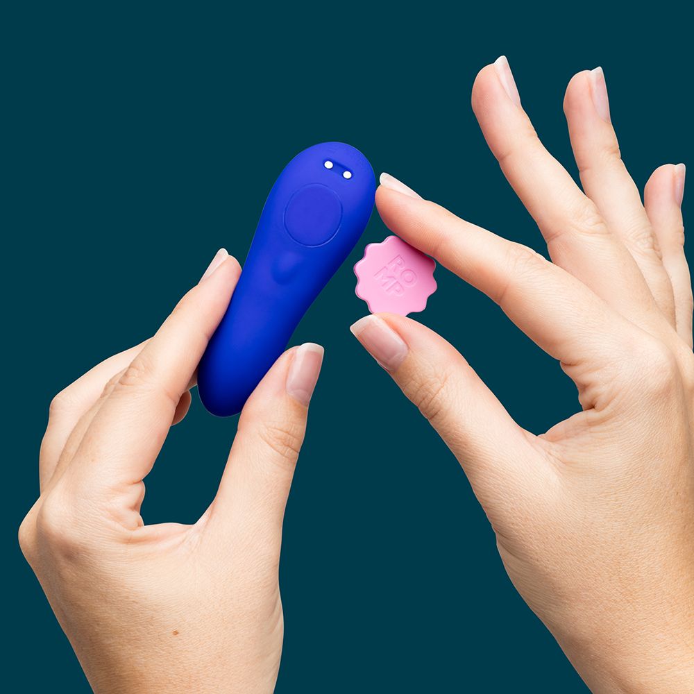 Blue electronic device held by hands with a pink flower-shaped object on a dark blue background