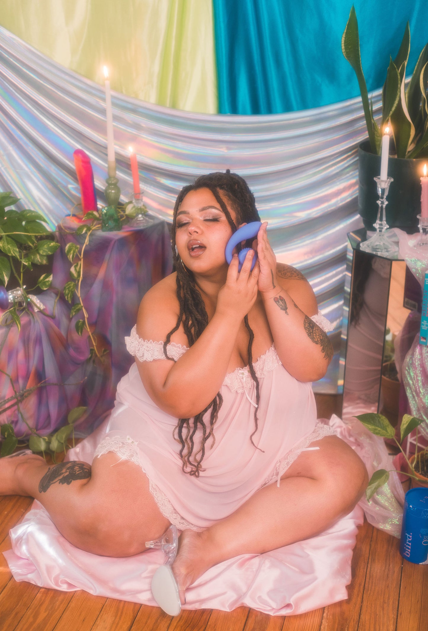 Woman in a white dress sitting on the floor with a colorful curtain and plants in the background