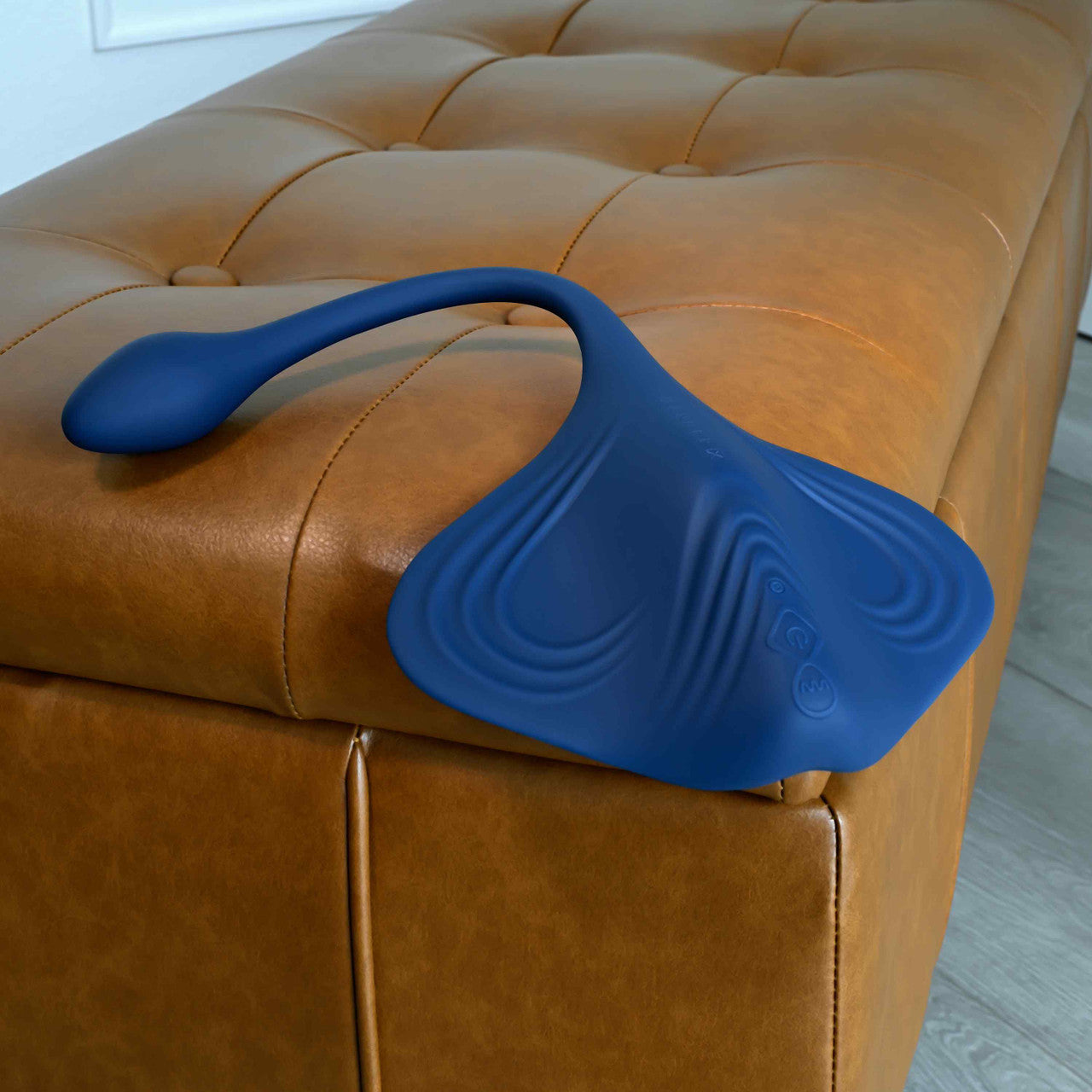 Blue silicone Gender X Daily Grind Vibrator on a brown leather couch