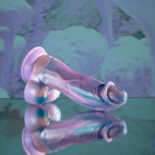 Mythical Silicone Vibrating Dildopink top on a reflective surface with a blurred abstract background