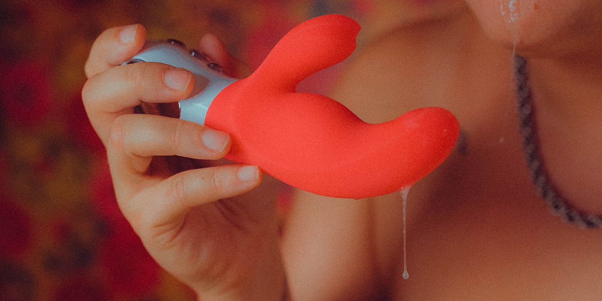 An anal-safe rabbit style vibrator with spit dripping from it being held by a queer person