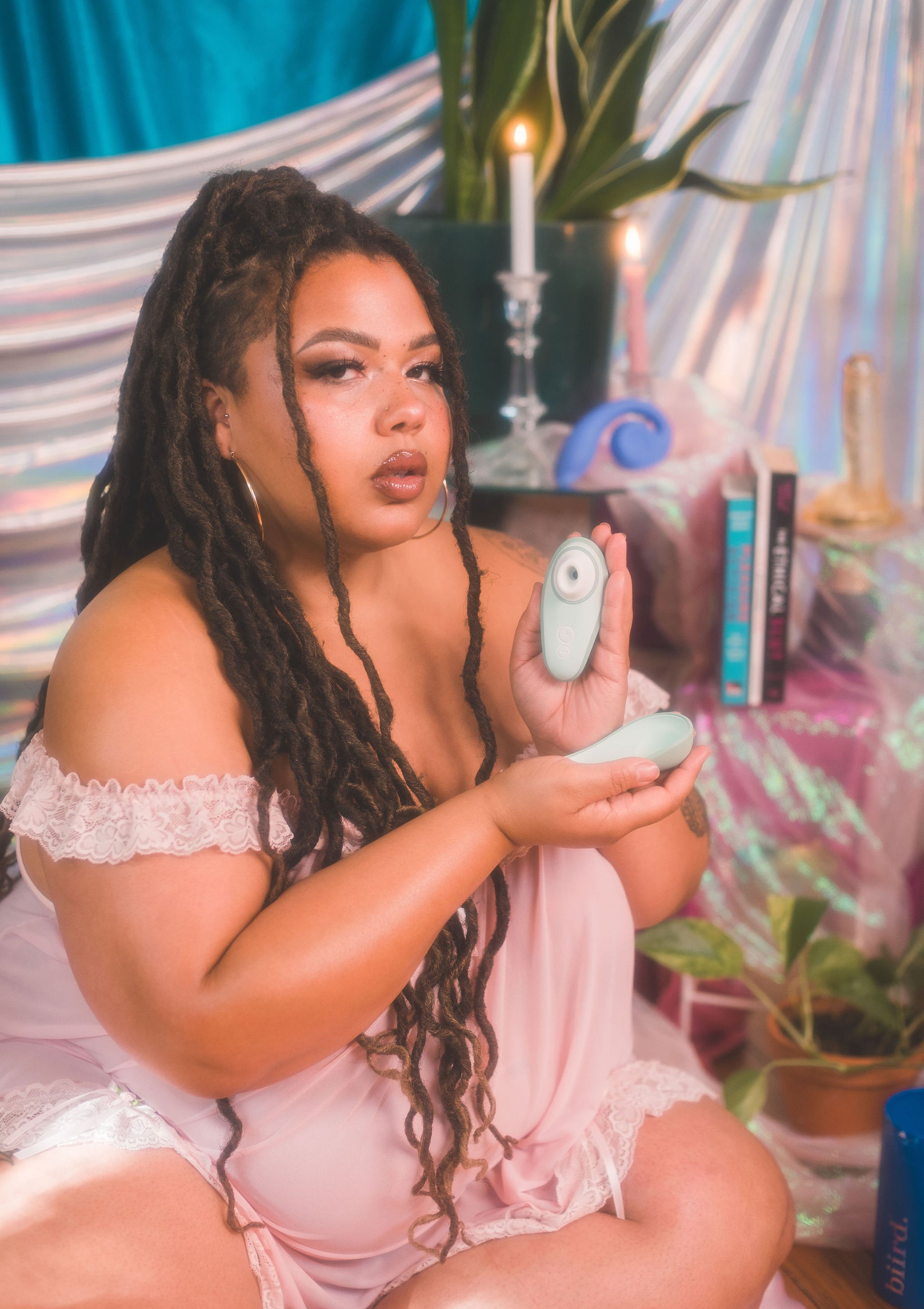 Woman holding a green Womanizer Liberty 2 in a decorative indoor setting with plants and candles.
