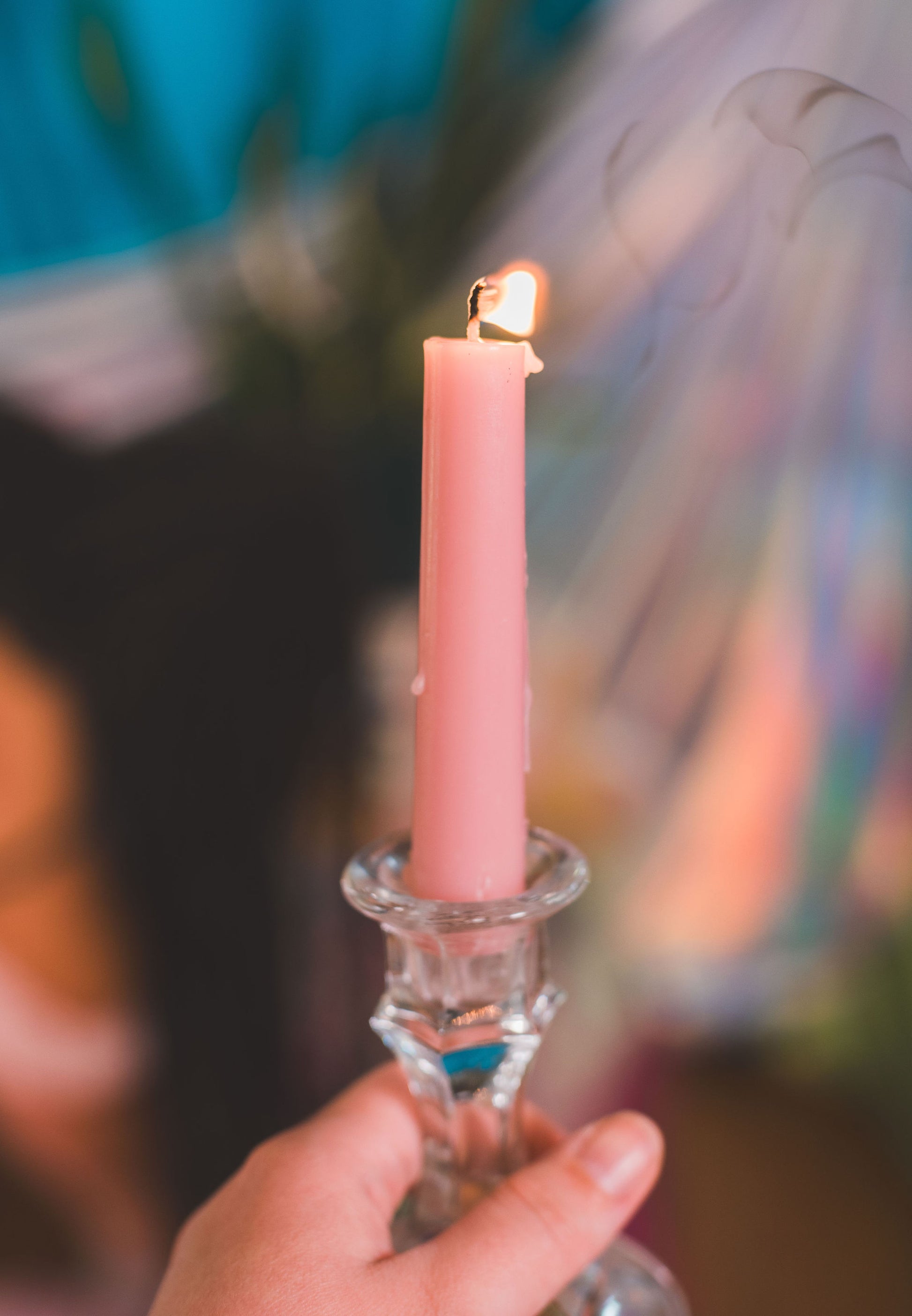 Hand holding a pink candle in a glass holder with blurred background