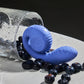 A blue vibrator with a snail-like design, placed next to a glass and scattered blueberries, indicating it's waterproof and splashproof.