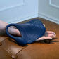 Blue silicone Gender X Daily Grind Vibrator held by a hand on a brown leather surface.