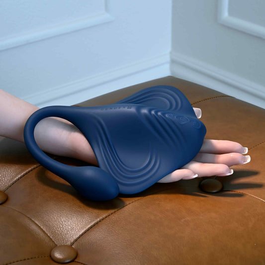 Blue silicone Gender X Daily Grind Vibrator held by a hand on a brown leather surface.