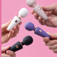 Four Le Wand Mini Micro Wand in white, purple, and black held by hands against a pink background.