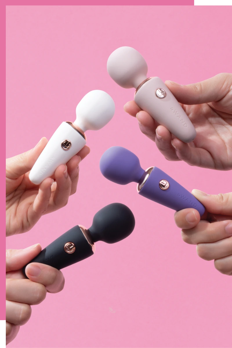 Four Le Wand Mini Micro Wand in white, purple, and black held by hands against a pink background.