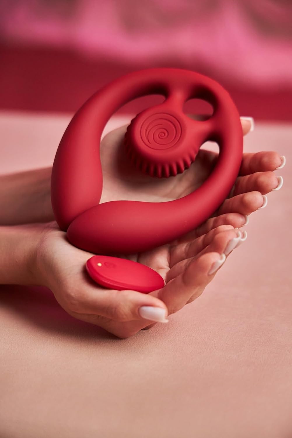 Red handheld SVibe Snail GIZI Duo Double Ended Dildo And Vibe held in hands against a pink background