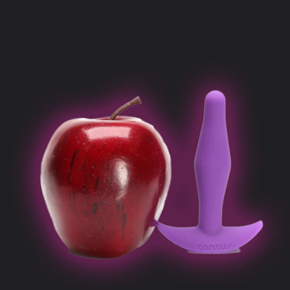 Red apple next to a purple Tantus Little Flirt Anal Plug 
