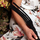 Person holding a black Tantus Tawse Paddle with floral-patterned clothing and plants in the background