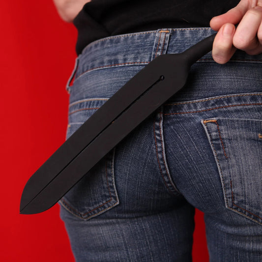 Person holding a black Tantus Tawse Silicone Paddle against a red background